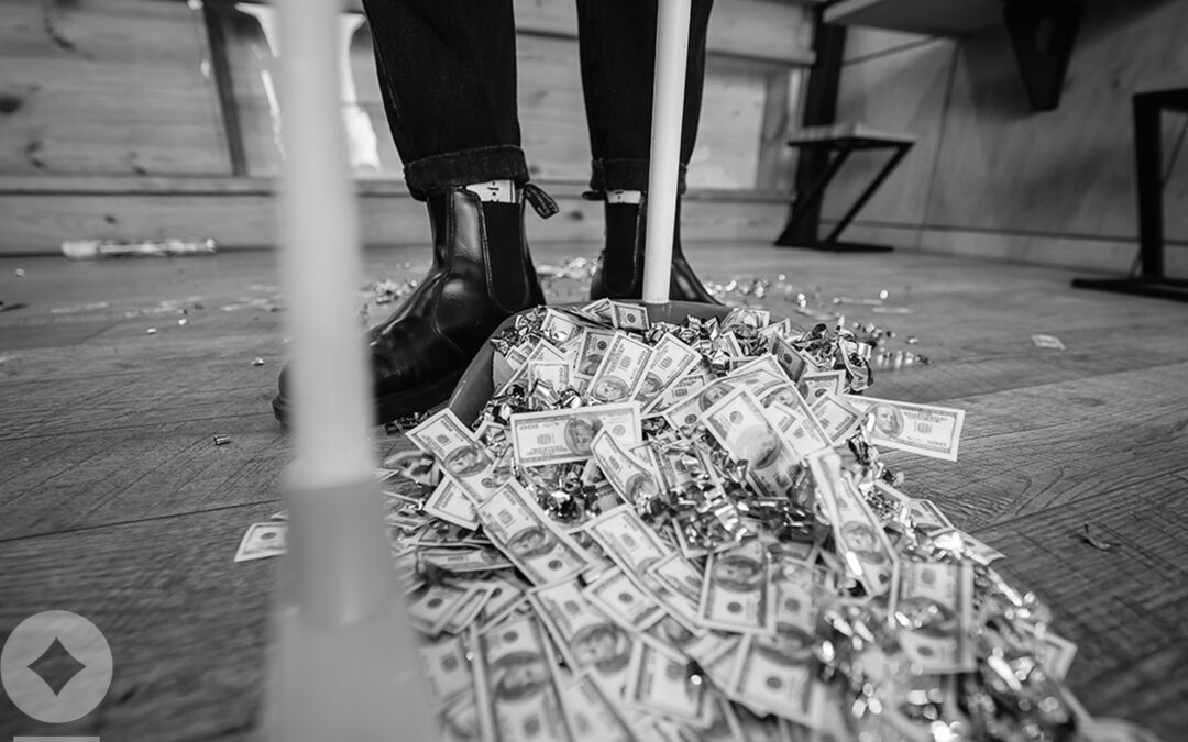 Broom sweeping dollars in scoop from on wooden floor